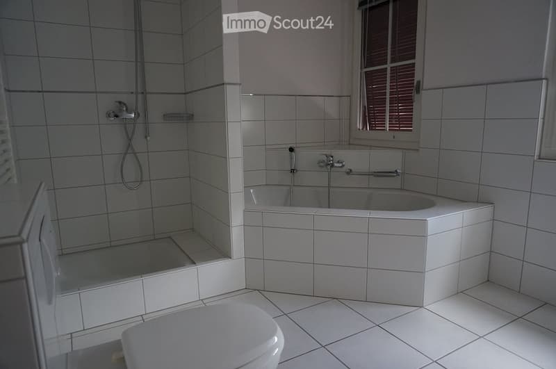 Modern bathroom with white tiled walls and floor, featuring a bathtub, toilet, and a separate shower area with a glass enclosure.