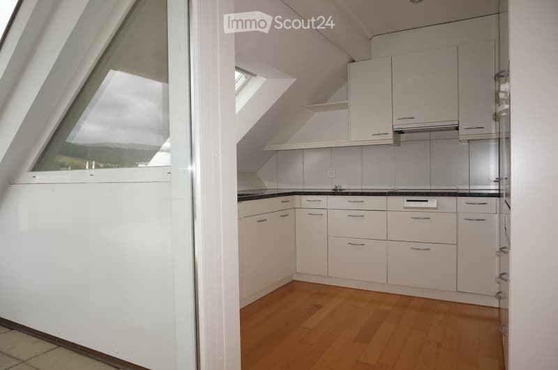 Modern kitchen with white cabinets, wooden flooring, and large windows offering a scenic view.