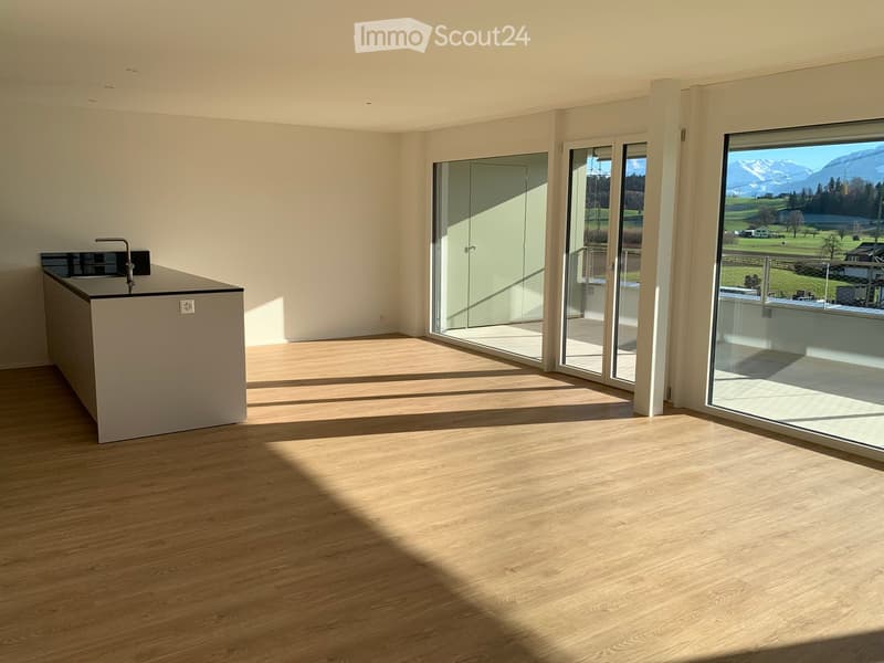 Empty room with light wooden flooring, white walls, and large glass sliding doors leading to a balcony with a scenic mountain view.