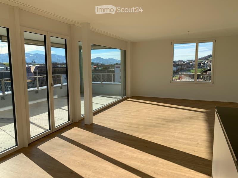 Empty room with wooden flooring, large glass sliding doors leading to a balcony, and windows offering a scenic mountain view.