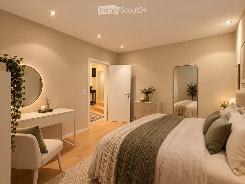 Modern bedroom with a large bed, a white vanity table, a round mirror, a small chair, and a drawer unit. The room features light wooden flooring and neutral-colored walls.