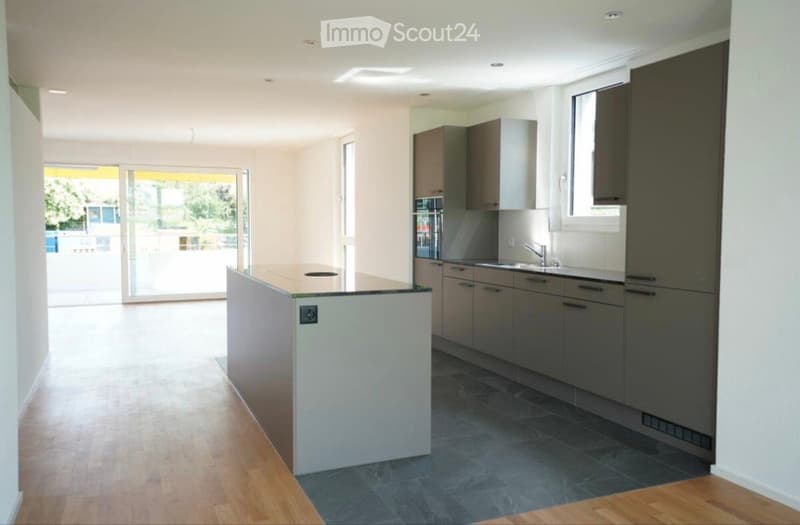Modern kitchen with light-colored cabinets, a central island, and a dark tiled floor. Features a sink with a modern faucet and ample natural light from large windows and a sliding glass door leading to an outdoor area.