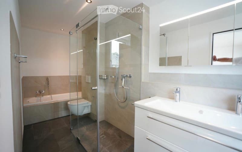 Modern bathroom with a glass-enclosed shower, bathtub, toilet, sink, and illuminated mirror.