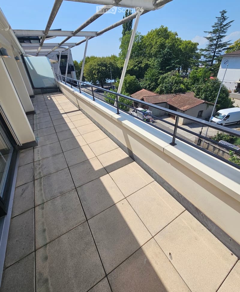 Balcony with tiled floor, metal railing, and a view of trees and buildings in the background.