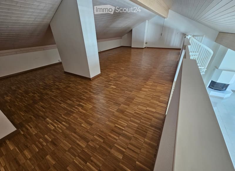 Empty room with wooden flooring and white walls, featuring a curved ceiling and a white railing leading to another area.