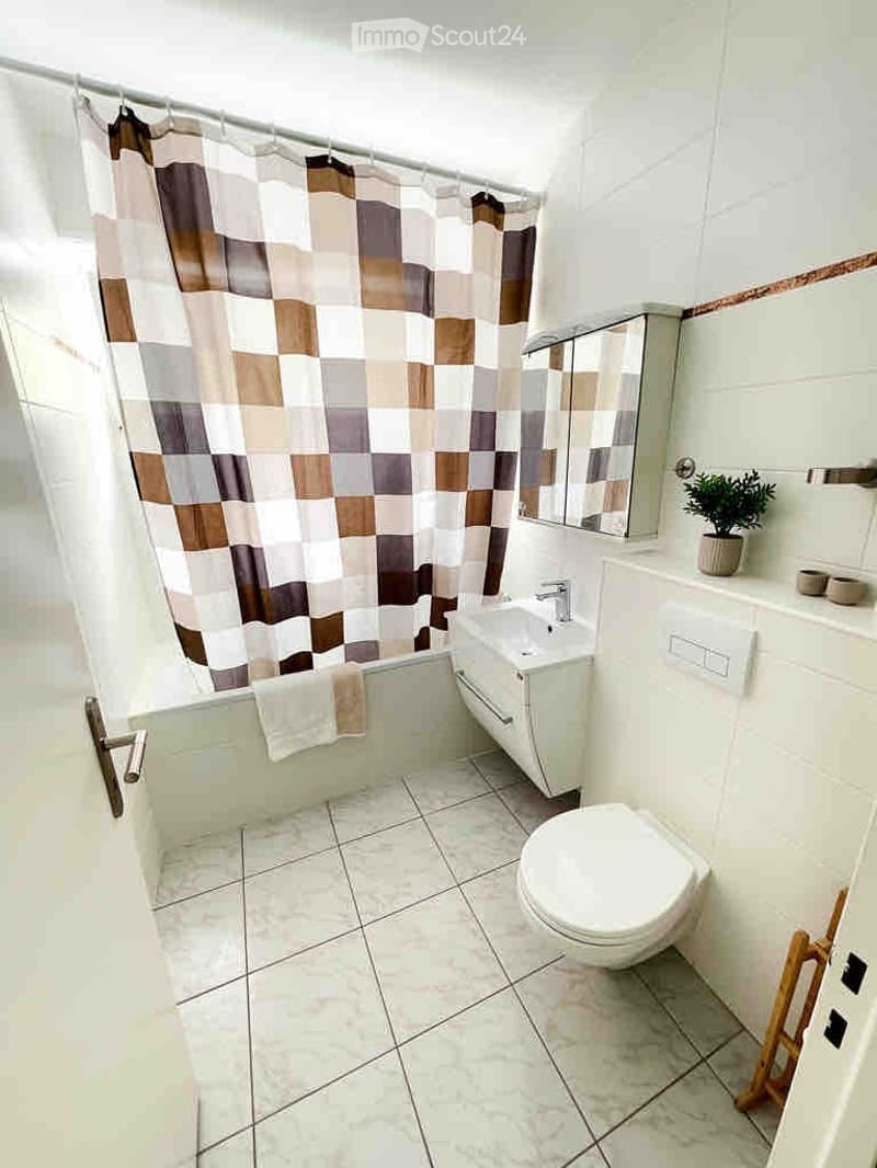Modern bathroom with white tiles, bathtub, toilet, sink, mirror, and a small plant on the counter.