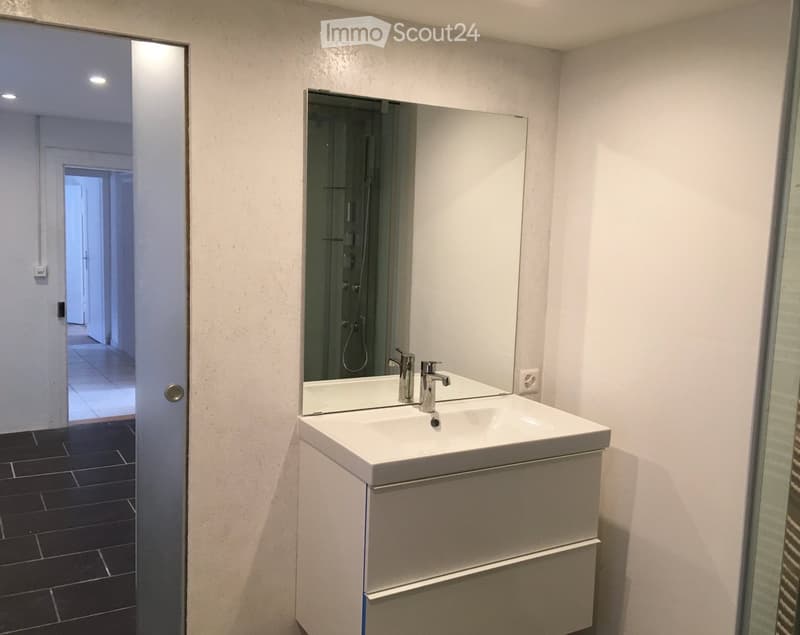 Modern bathroom with a white sink, large mirror, and chrome faucet. Dark tiled floor and white walls.