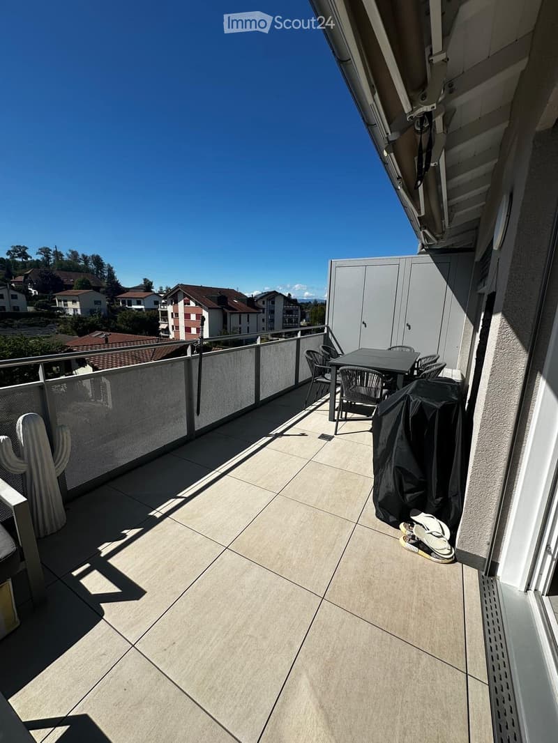 Balcony with tiled floor, metal railing, small table and chairs, covered grill, and a cactus plant.