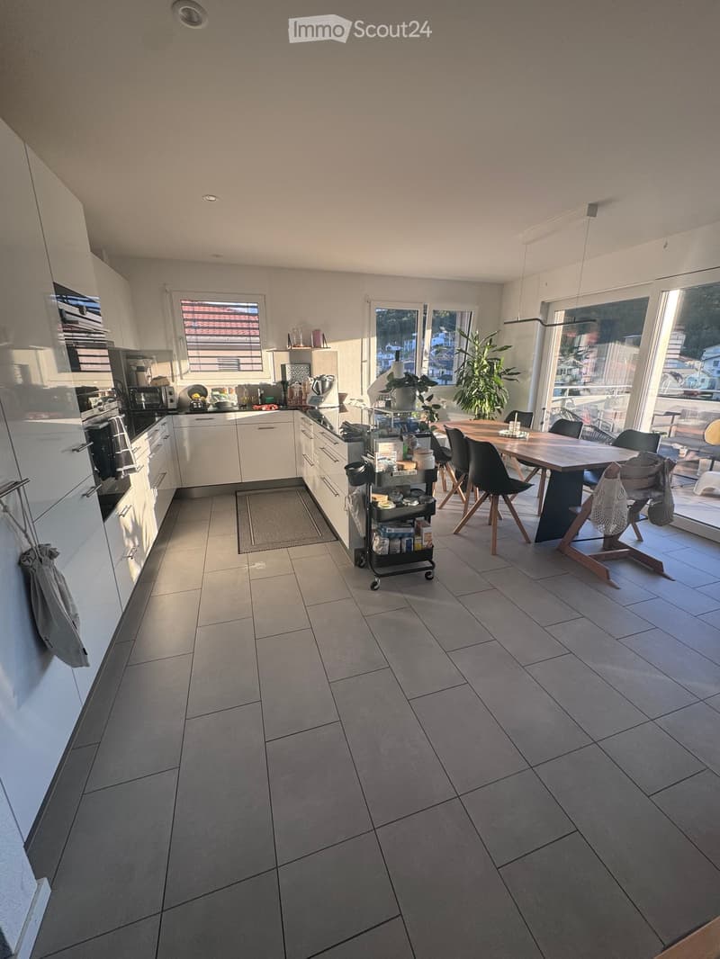 Modern kitchen with white cabinets, stainless steel appliances, a dining table with chairs, and a cart with various items.