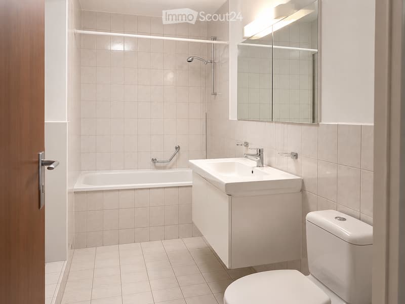 Modern bathroom with beige tiles, a bathtub, a sink with a modern faucet, a toilet, and a large mirror with built-in lighting.
