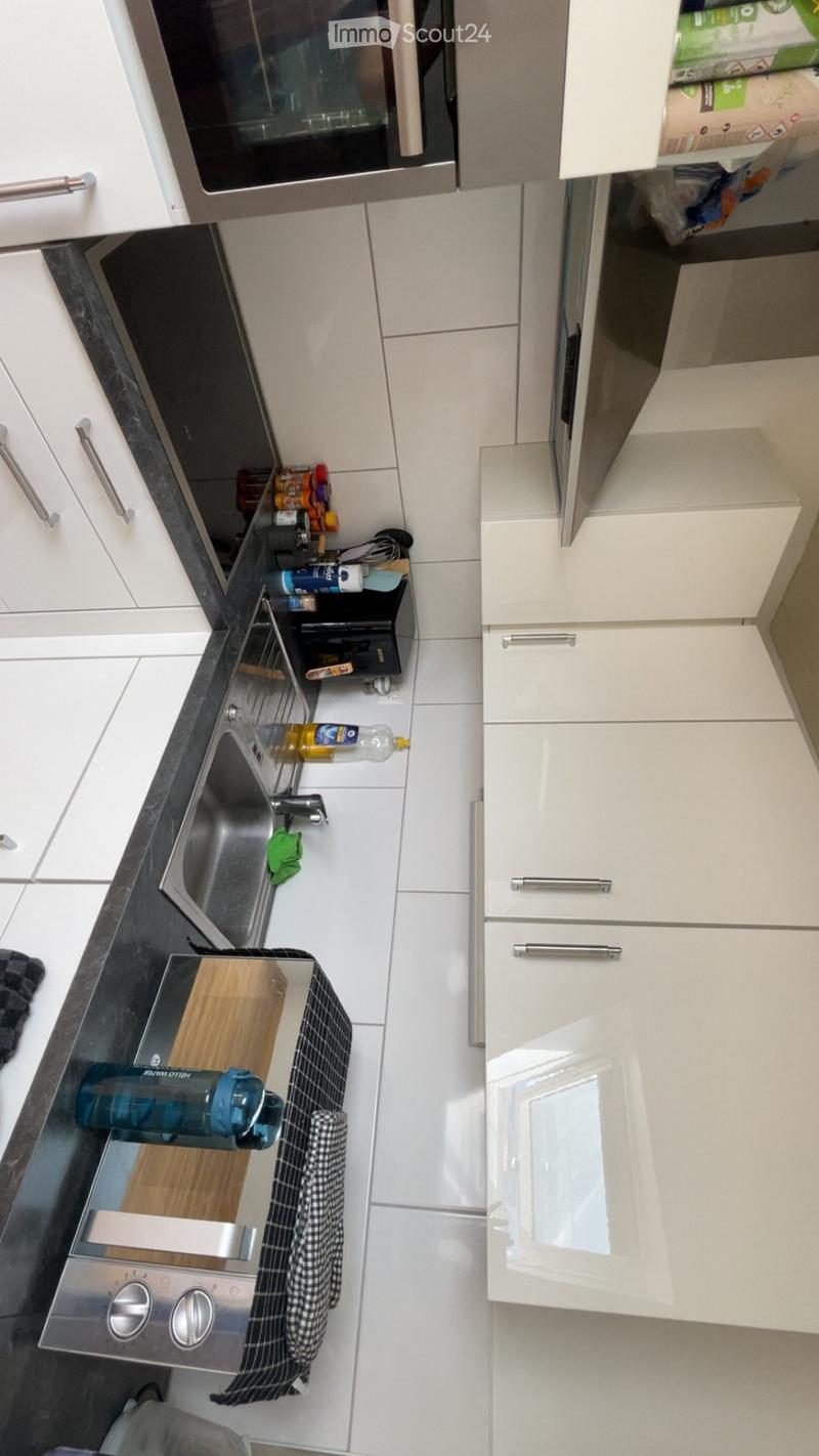 Modern kitchen with white cabinets, stainless steel appliances, and a black countertop. Visible items include a sink, oven, microwave, and various kitchen utensils.