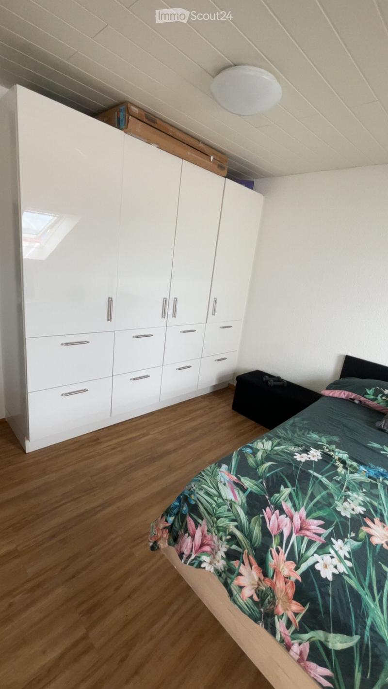 Bedroom with wooden flooring, white built-in wardrobe, bed with floral duvet, and a small black stool.