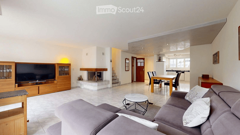 Modern living room with a grey sectional sofa, coffee table, fireplace, TV, dining area, and wooden cabinetry.