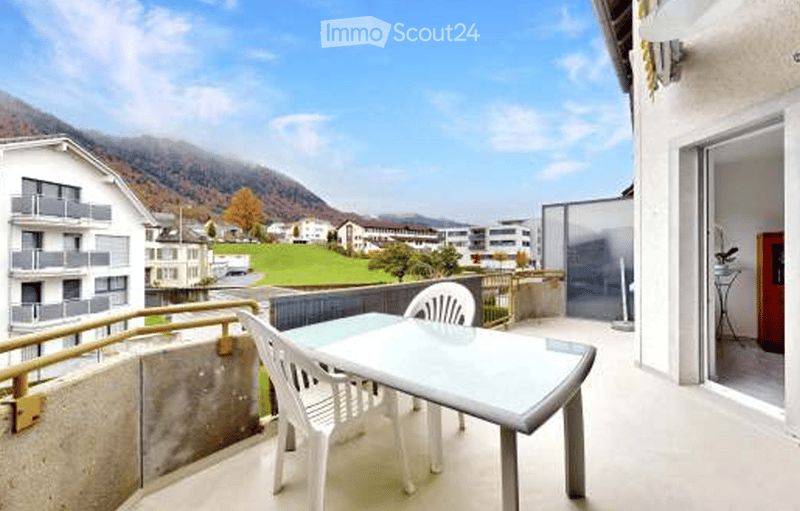 Balcony with a table and chairs, overlooking a scenic mountain view and a residential area.