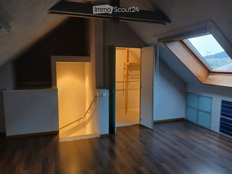 Empty attic space with wooden flooring, exposed wooden beams, skylight window, and open closet area.