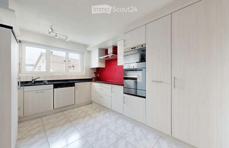 Modern kitchen with white cabinets, black countertops, stainless steel appliances, and a red accent wall.