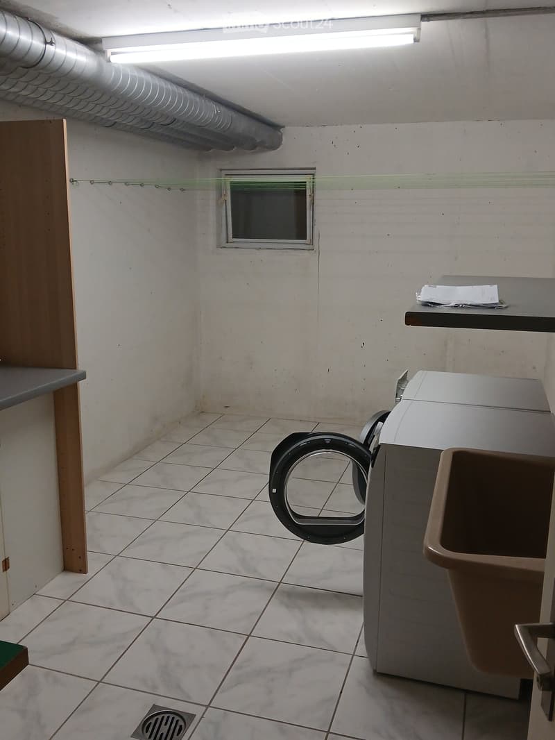 Empty room with tiled floor, white walls, a small window, and a washing machine with a drum paddle. No furniture or personal items are present.