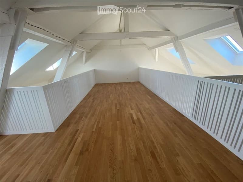 Empty room with wooden flooring, white walls, and skylight windows in the ceiling.