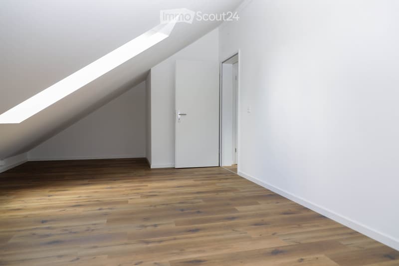 Empty attic space with wooden flooring, white walls, and skylight windows allowing natural light. Two white doors are visible, one leading to another room.