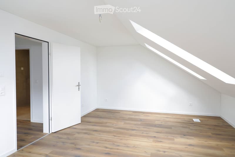 Empty attic room with wooden flooring, white walls, and skylight windows allowing natural light. No furniture or equipment present.