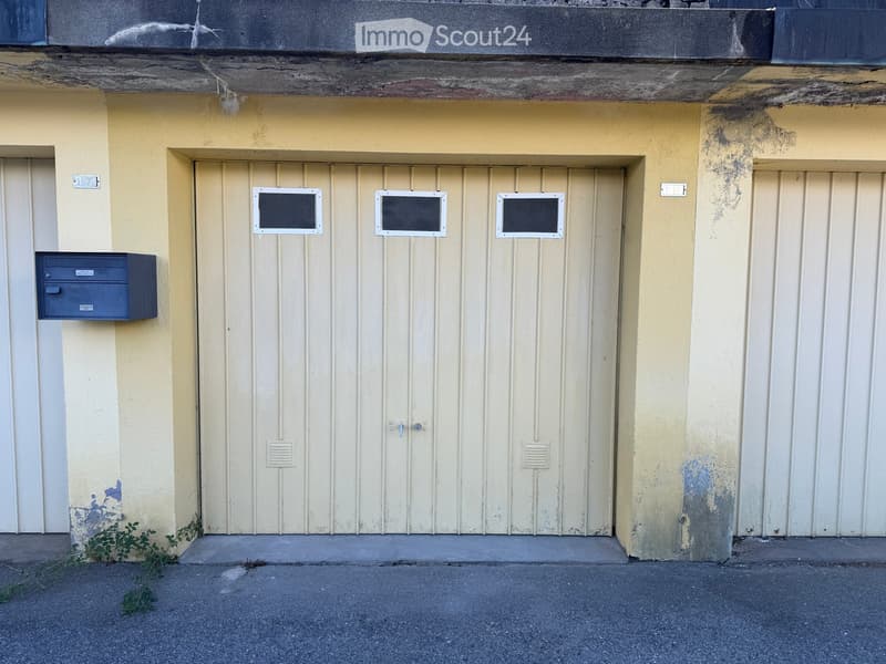 Exterior view of a building with a closed garage door, mailboxes, and small windows above the door.