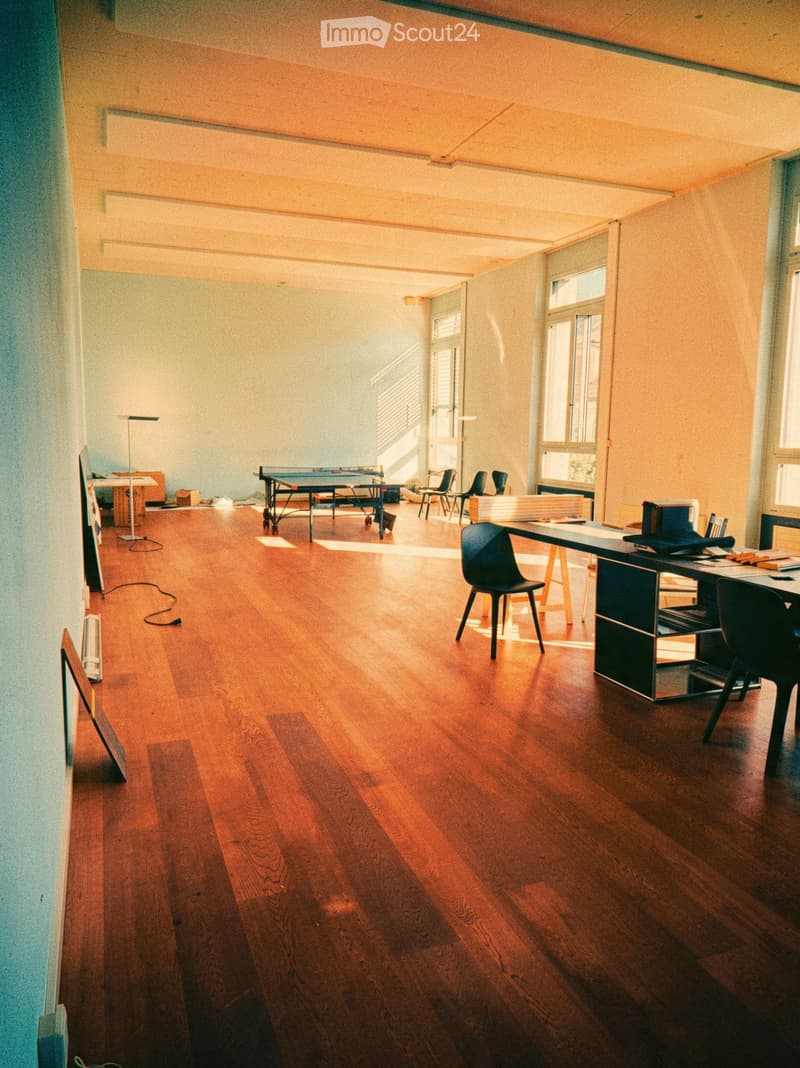 Open, well-lit room with wooden flooring, a ping pong table, a desk with chairs, and a screen on the wall.