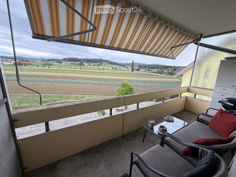 Balcony with a view of a rural landscape, featuring a lounge chair, small table, and cups.