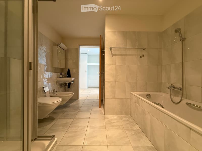 Modern bathroom with beige tiles, a bathtub, shower, toilet, sink, and a mirrored cabinet.
