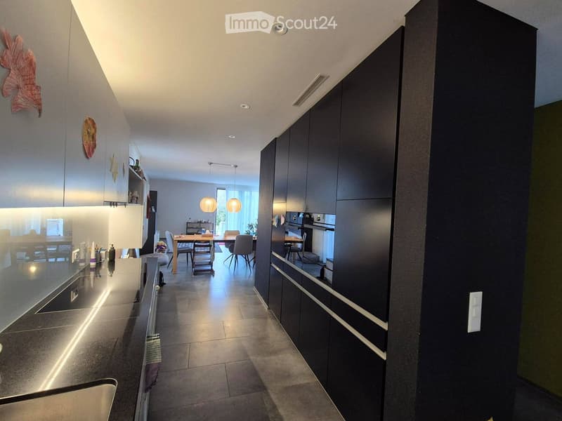 Modern kitchen with dark cabinets, a central island, and a dining area with a table and chairs.