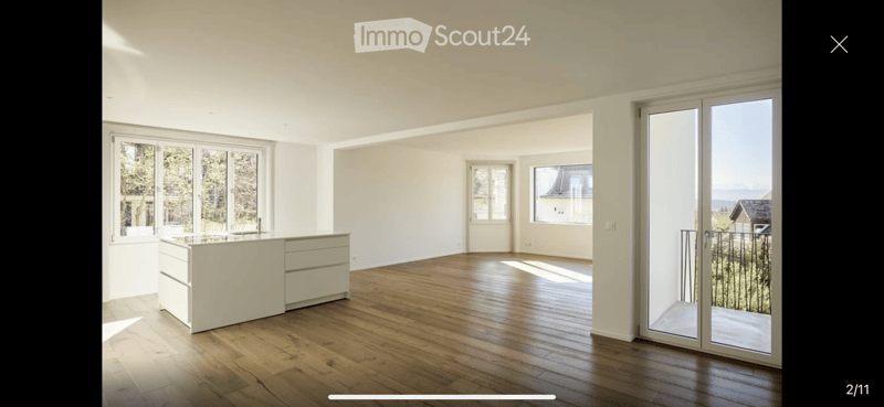 Bright, unfurnished room with wooden flooring, large windows, and a sliding glass door leading to a balcony with scenic views.