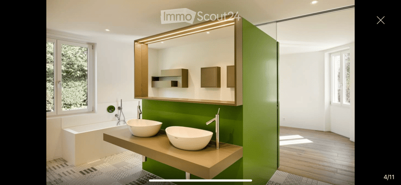 Modern bathroom with a green accent wall, double sink vanity, bathtub, and built-in mirrored cabinet with lighting.