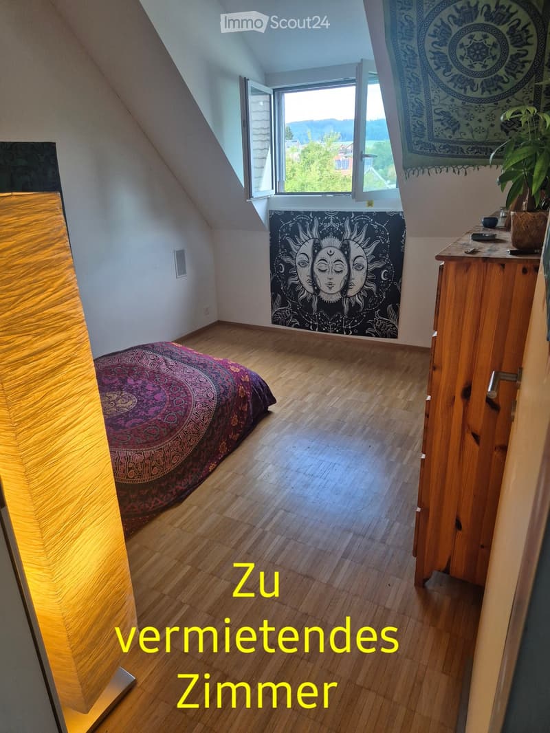 Bright, wooden-floored bedroom with a bed, a small wooden table with a plant, and large windows offering a scenic view.
