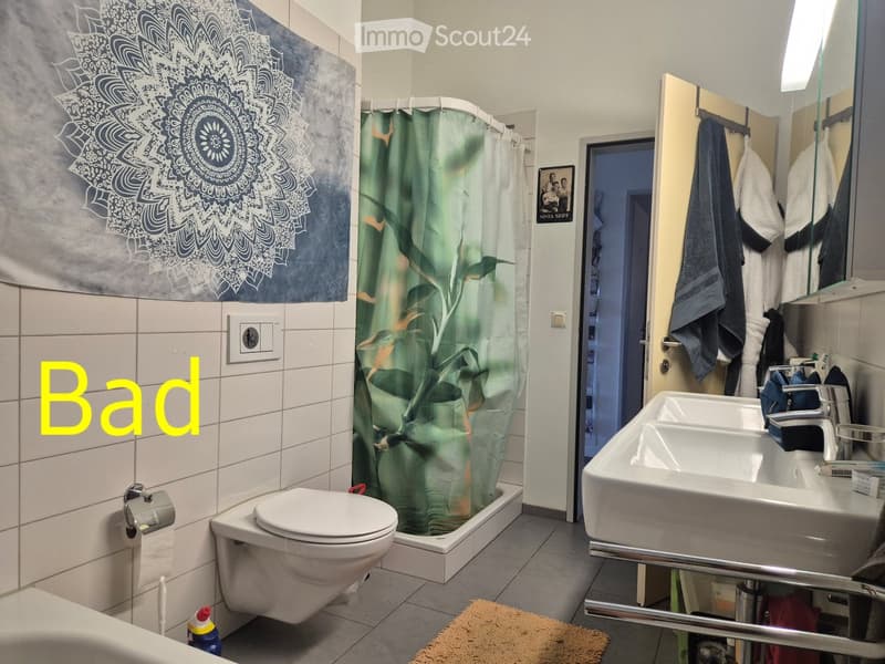 Modern bathroom with white tiles, a toilet, a sink, a bathtub with a green leaf-patterned shower curtain, a mirror, and towels hanging on a rack.
