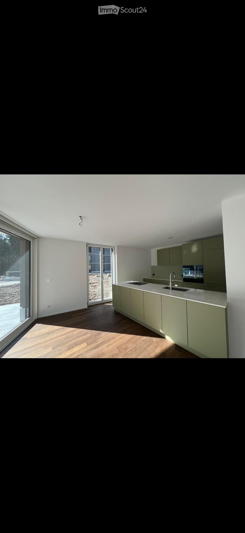 Modern kitchen with light green cabinets, a marble countertop, and a stainless steel sink. Large windows and sliding glass doors provide natural light and access to the outdoor area.