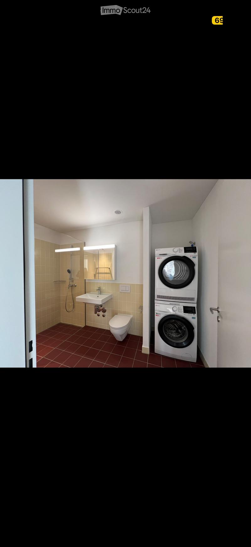 Modern bathroom with a sink, toilet, mirror, shower, and a stacked washing machine and dryer unit.