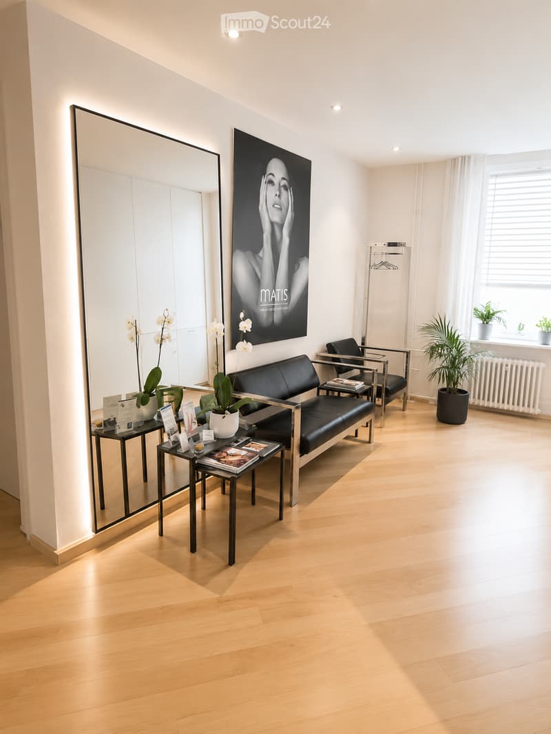 Modern, minimalist room with light wooden flooring, a black leather sofa, a matching chair, small side tables, a large mirror, and a large artwork on the wall.