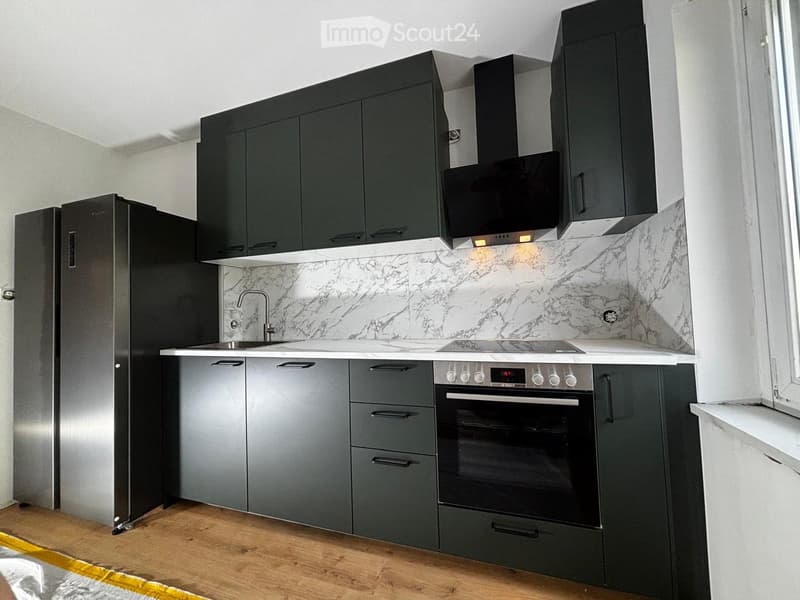 Modern kitchen with dark grey cabinets, marble backsplash, stainless steel appliances, and wooden flooring.