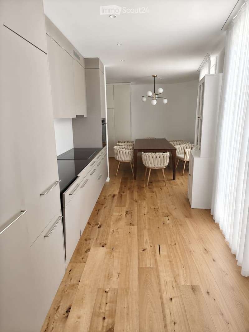 Open-plan kitchen and dining area with light wood flooring, white cabinets, and a modern chandelier.
