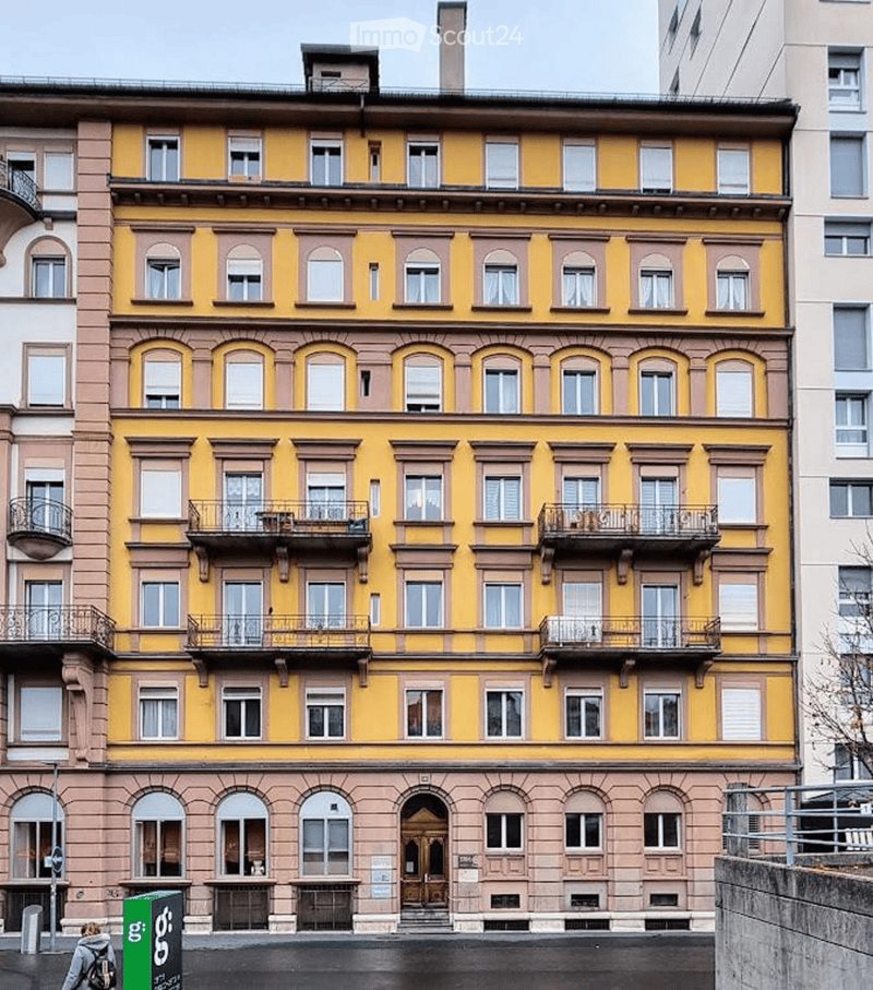 A multi-story residential building with yellow and pink facade, multiple windows, balconies, and ornate architectural details.