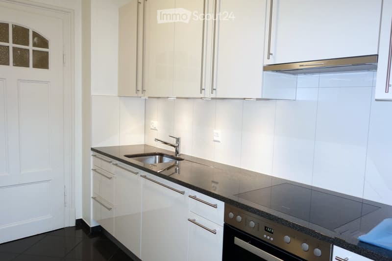Modern kitchen with white cabinets, stainless steel appliances, and a black countertop.