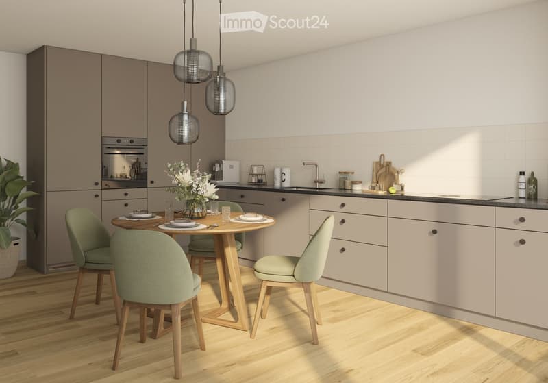 Modern kitchen with light-colored cabinets, a round wooden dining table with four green chairs, a vase with white flowers, and various kitchen items on the counter.