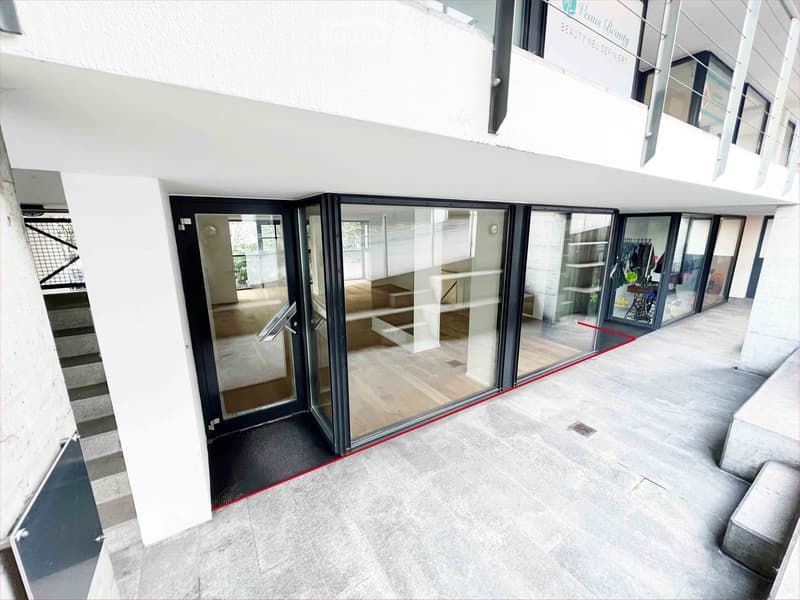 Modern hallway with large glass sliding doors leading to an interior space, concrete floors, white walls, and a staircase visible on the left side.