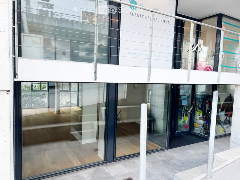 Modern building entrance with large glass doors and a balcony above, featuring signage for "BEAUTY NEL" and website details.