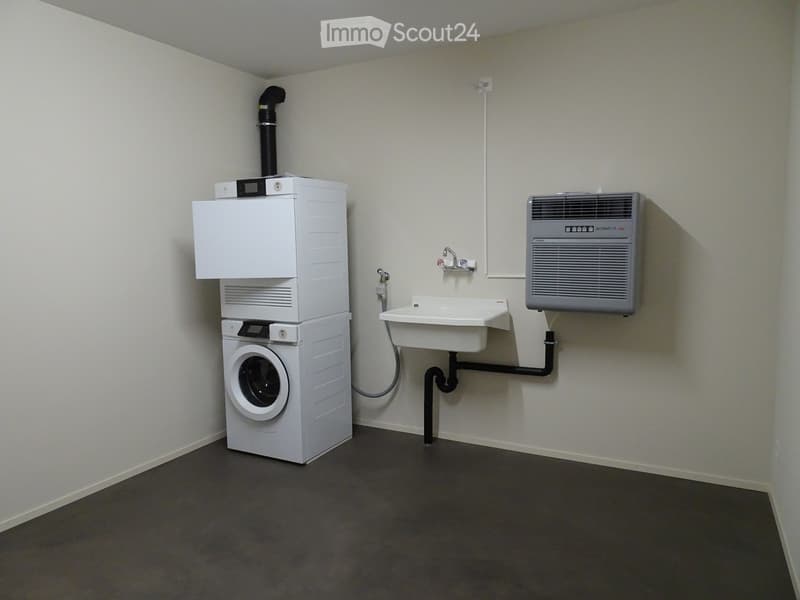 A small utility room with a stacked washing machine and dryer, a sink with a faucet, and an air conditioner mounted on the wall.