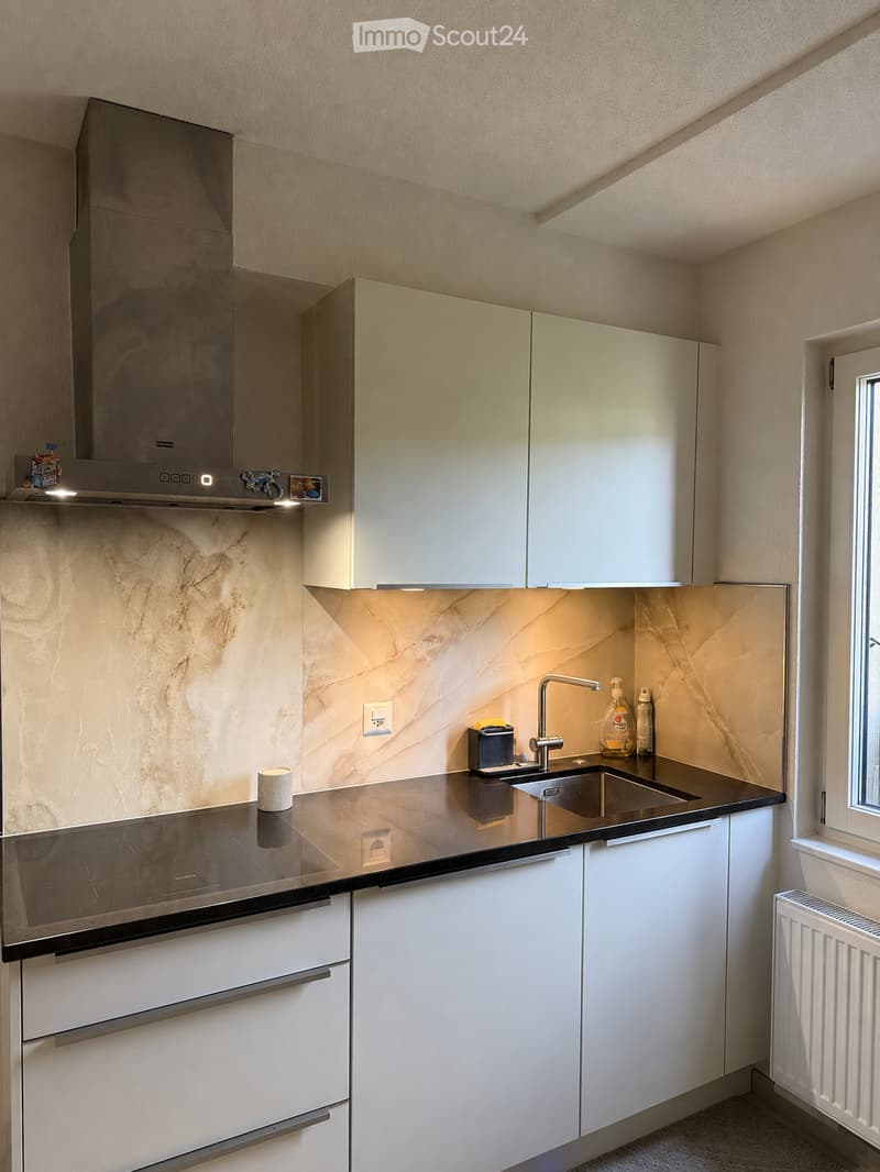 Modern kitchen with white cabinets, marble backsplash, stainless steel range hood, and a black countertop.