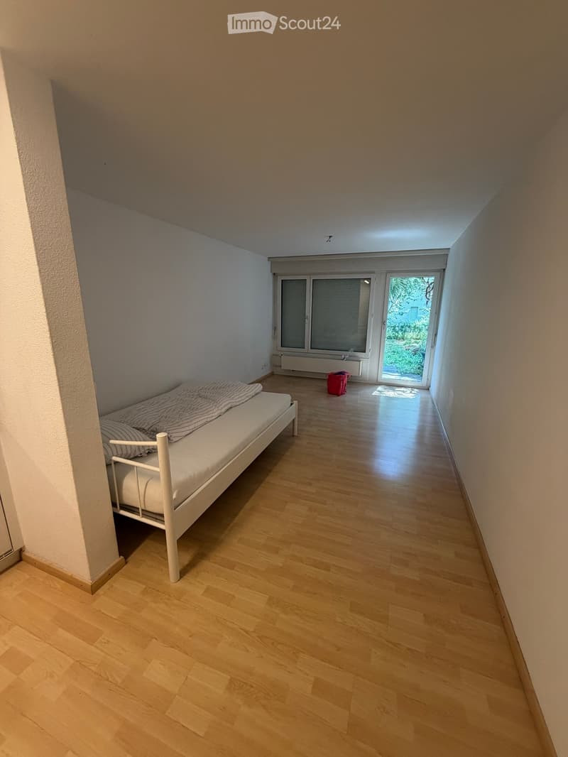Small bedroom with wooden flooring, white walls, a single bed with striped bedding, a radiator, and a sliding glass door leading to a balcony.