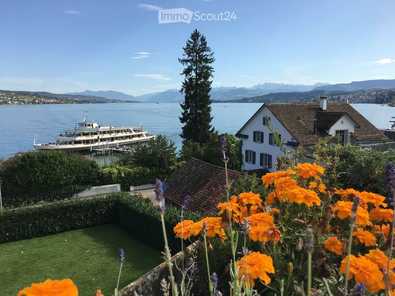 Garden with orange flowers and lavender, overlooking a lake with a docked boat and distant mountains.