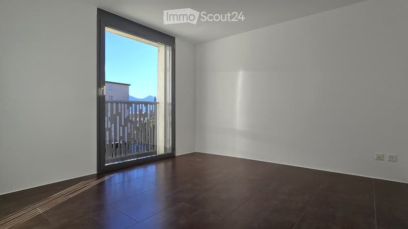Empty room, white walls, sliding glass door to balcony, brown tiles, power outlets on the wall.