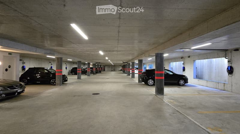 A few cars parked, multiple charging stations, pillar for support, wide passage.