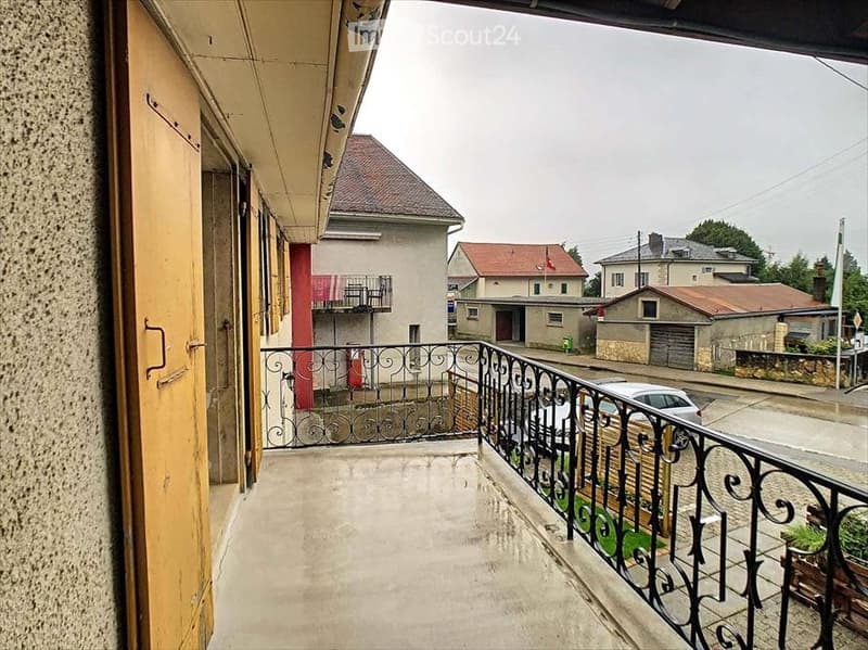 Balcony with metal railing, overlooking a residential street with houses and parked cars.